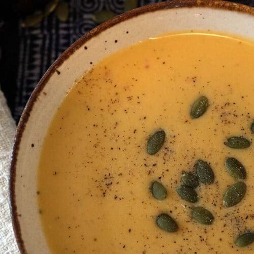 A bowl of curried apple and butternut squash soup topped with pumpkin seeds with a cream napkin