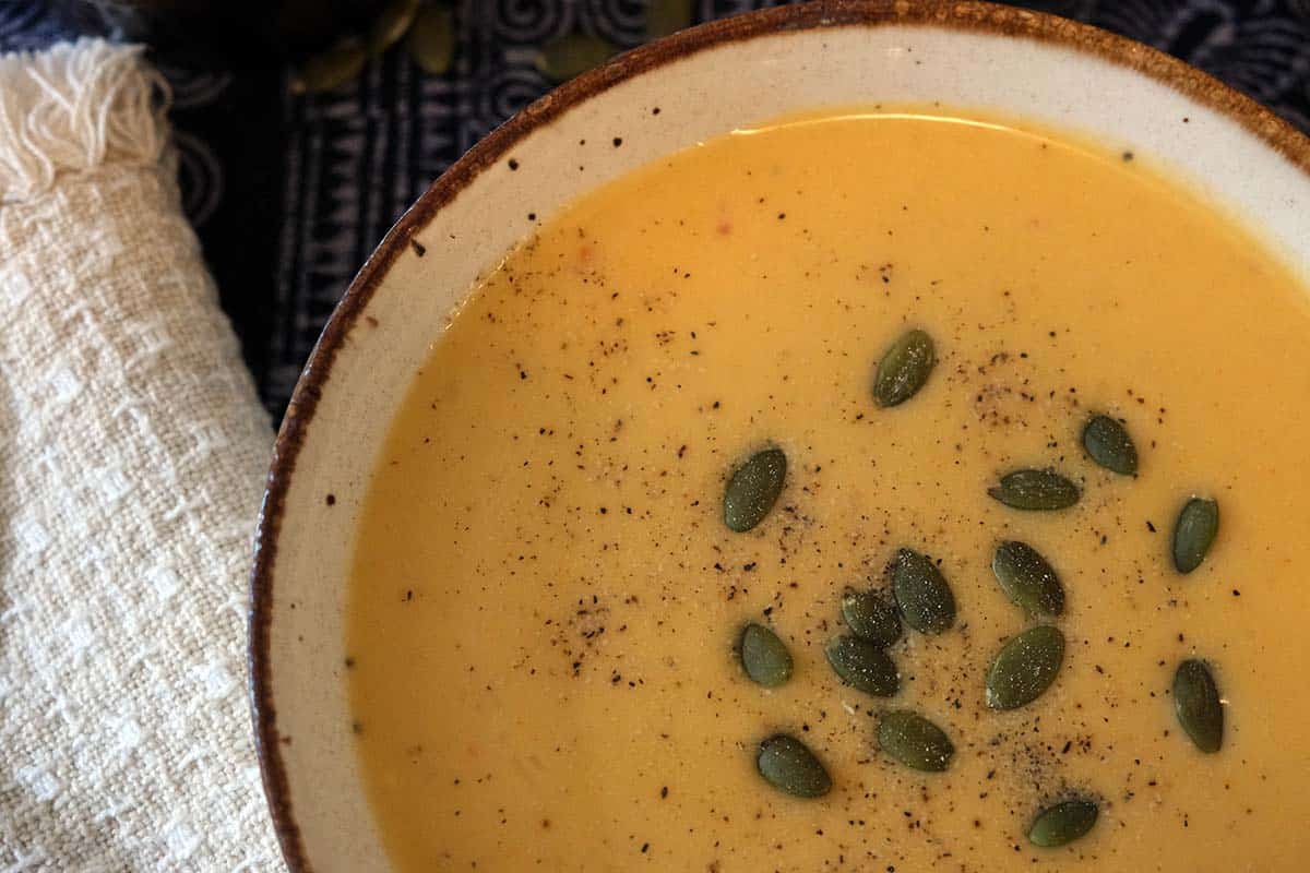 A bowl of curried apple and butternut squash soup topped with pumpkin seeds with a cream napkin