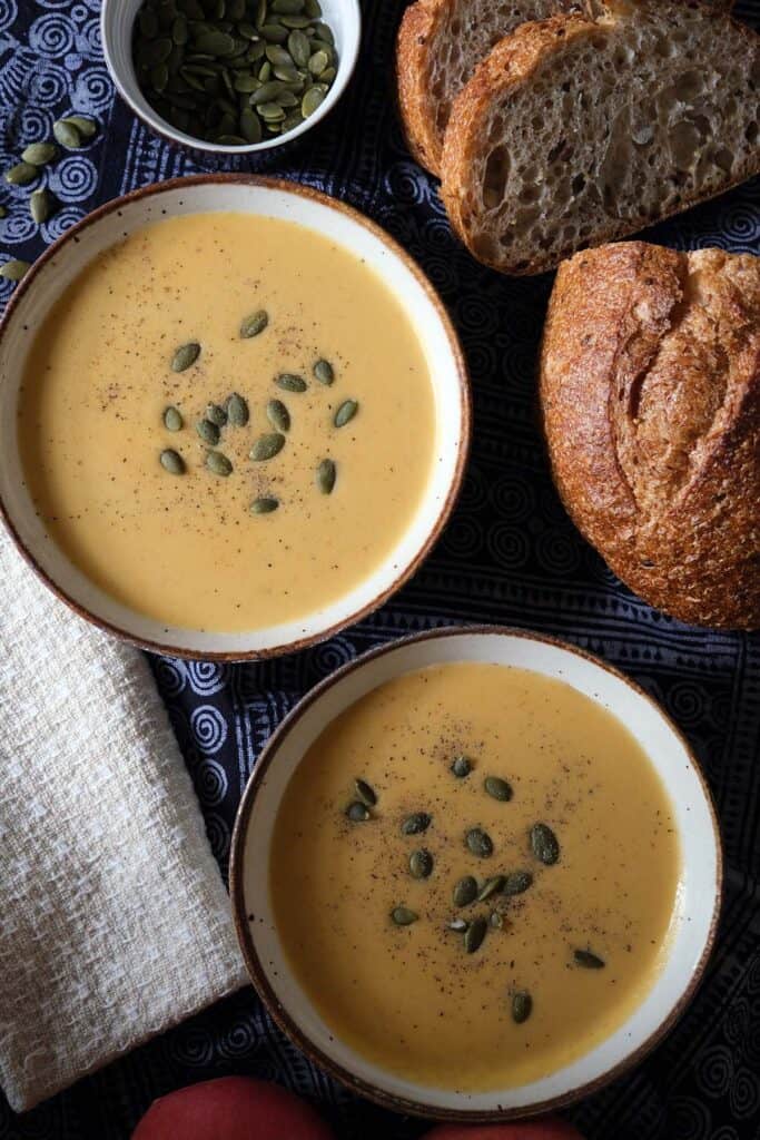 Curried apple and butternut squash soup recipe shown with two bowls, garnished with pumpkin seeds and paired with rustic bread.