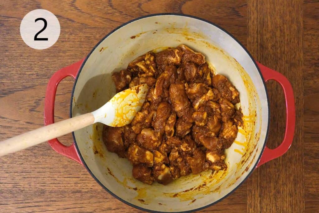 Chicken thighs being added to the fragrant curry paste in a skillet for Thai Massaman Curry.