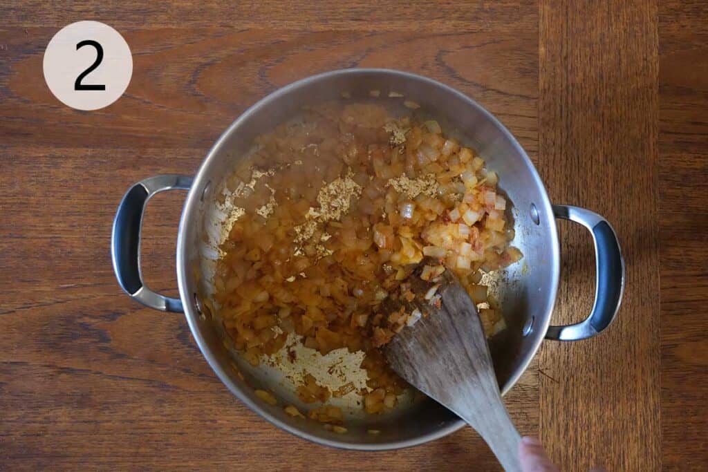 Sliced onions sautéing with Thai red curry paste in a soup pot, creating the flavorful base for curried apple and butternut squash soup.