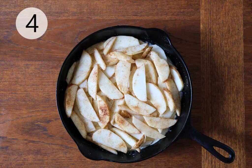 Layering cinnamon apples int a cast-iron skillet. the start of a golden puffed German Apple Pancake.