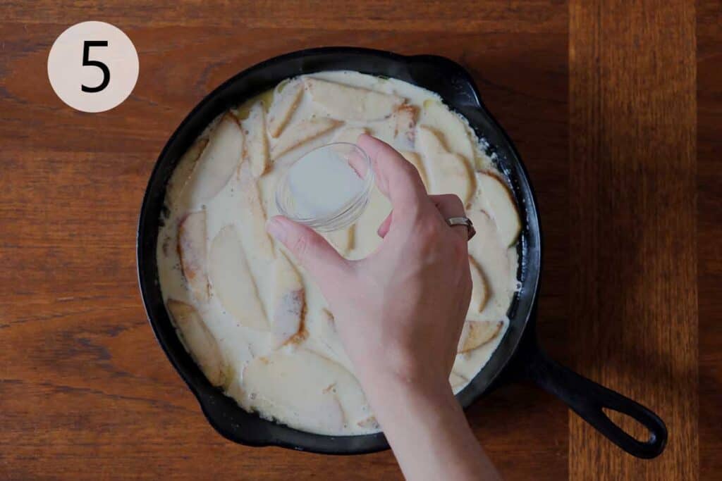 Sliced apples tossed in cinnamon and nutmeg in a medium bowl, ready to layer into a warm and fragrant German Apple Pancake.