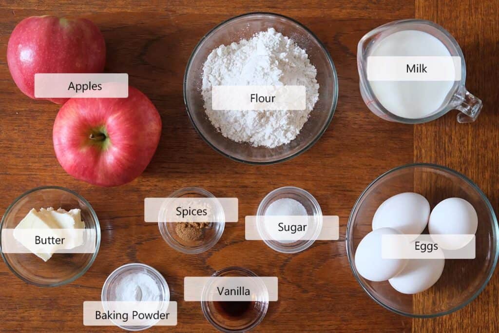Overhead view of wholesome ingredients for a German Apple Pancake Recipe, including apples, eggs, milk, and cinnamon on a wooden table. Simple staples for a cozy weekend brunch.
