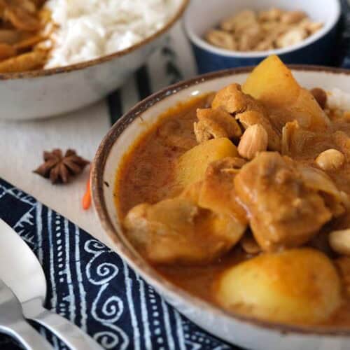 Creamy Chicken Massaman Curry with tender chicken, buttery potatoes, and roasted peanuts served over jasmine rice in bowls, styled with a blue napkin and spices.