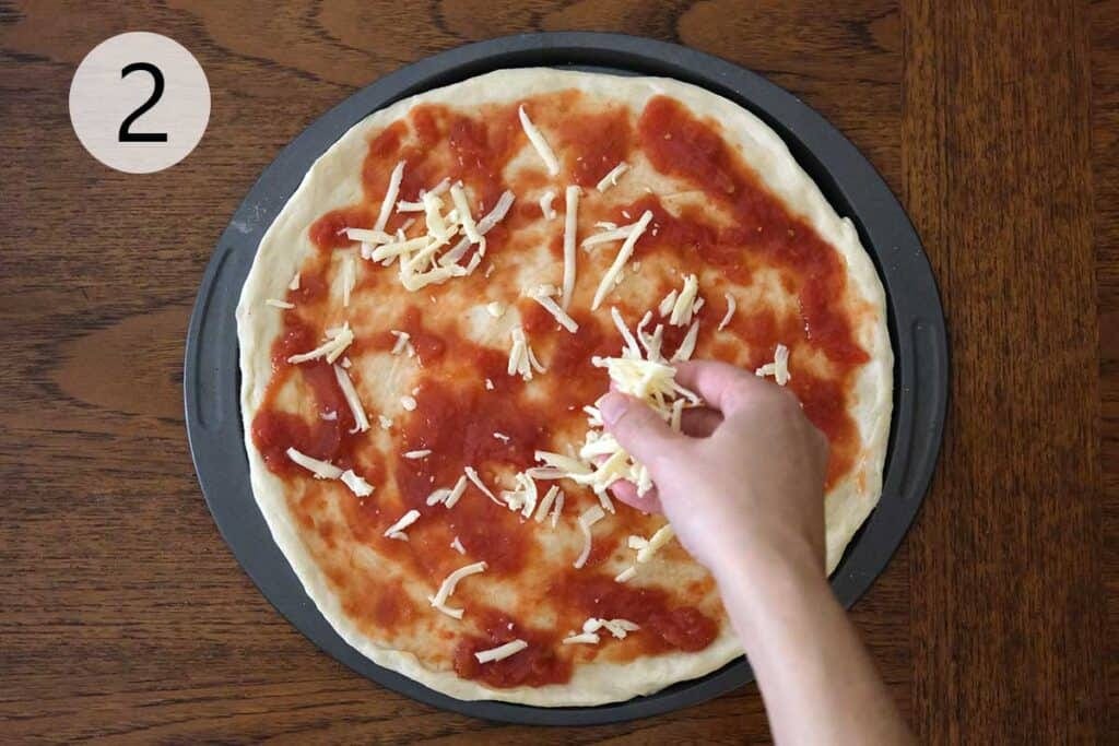 Sprinkling freshly grated mozzarella cheese overtop of tomato sauce.
