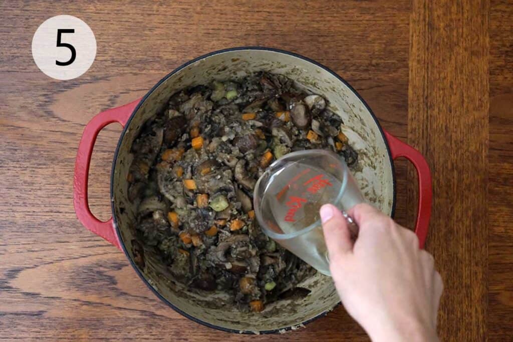 White wine poured into the pot to deglaze and wild rice added to simmer with vegetable stock for hearty mushroom soup flavor.