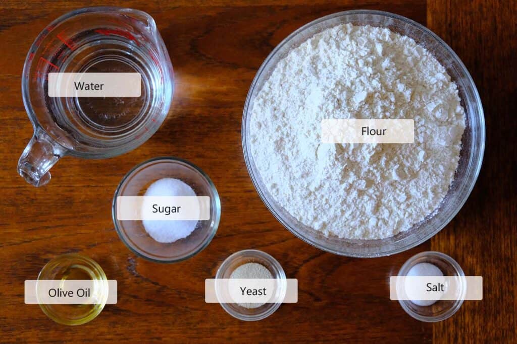 Ingredients for a thin crust pizza dough recipe including flour, yeast, salt, water, and sugar on a wooden table ready for mixing homemade pizza dough