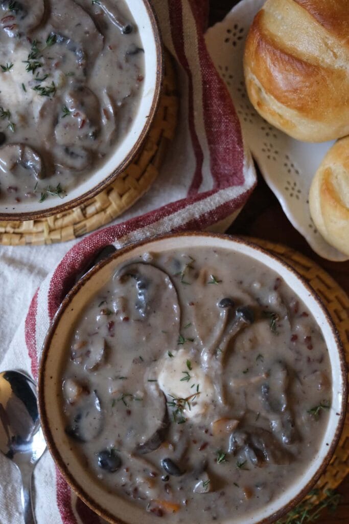Cozy table scene featuring bowls of creamy wild mushroom soup recipe with sour cream and thyme garnish.