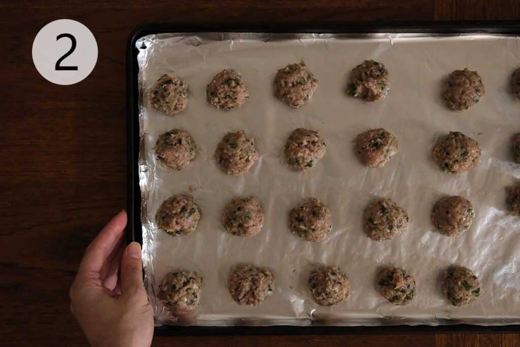 Raw turkey meatballs shaped on a foil-lined baking sheet before broiling for Turkey Meatball Soup Recipe.