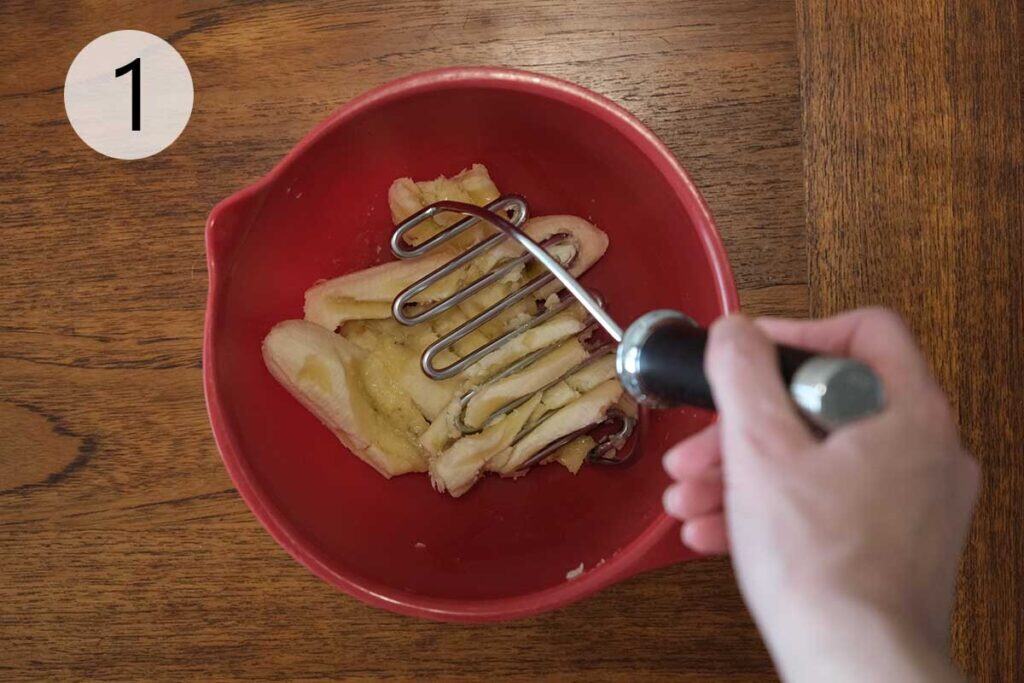 Ripe bananas being mashed in a mixing bowl to make whole wheat banana pancake batter.