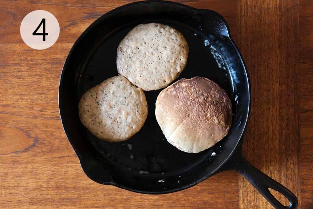 Whole wheat banana pancakes cooking in a skillet, bubbles forming on the surface before flipping.