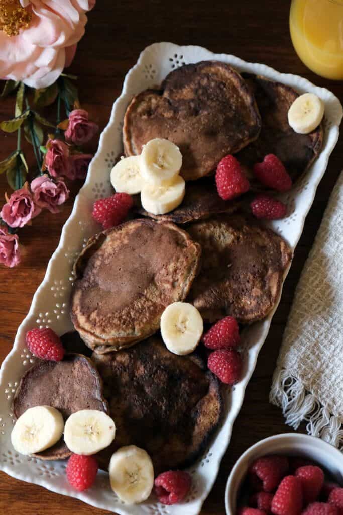 Close-up of whole wheat banana pancakes layered with bananas and berries, topped with maple syrup and served with fresh orange juice.