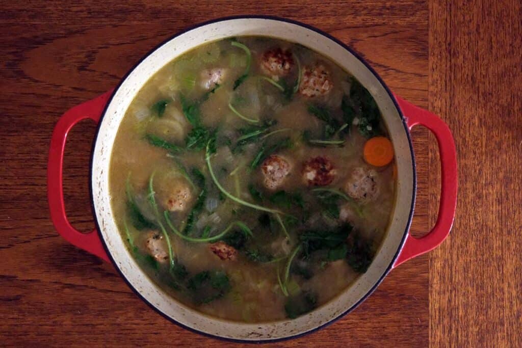 A large soup pot of fresh homemade turkey meatball soup on a wooden table.