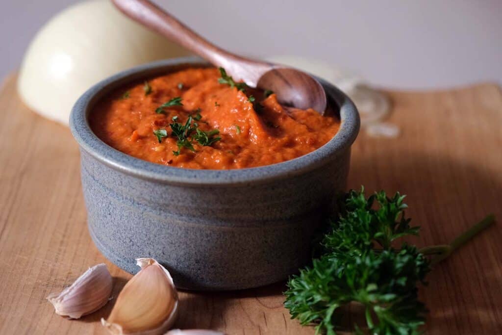 Ajvar recipe finished red pepper and eggplant spread in a rustic bowl garnished with parsley and garlic