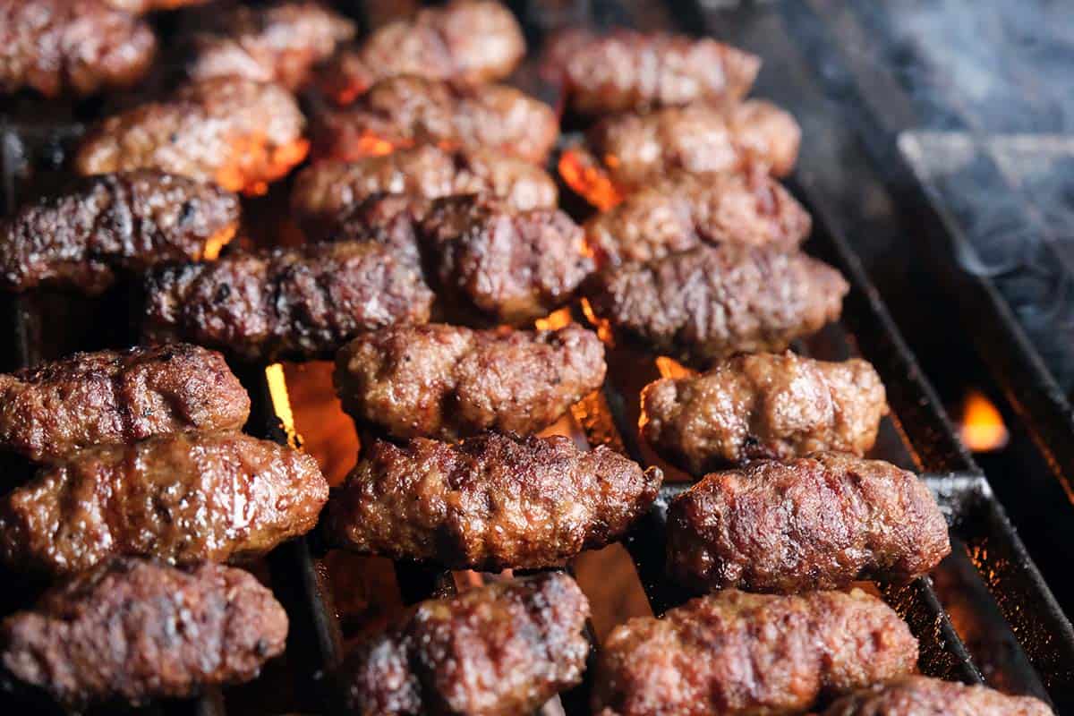 Ćevapčići grilling over open flame showing charred Balkan sausages cooking on barbecue