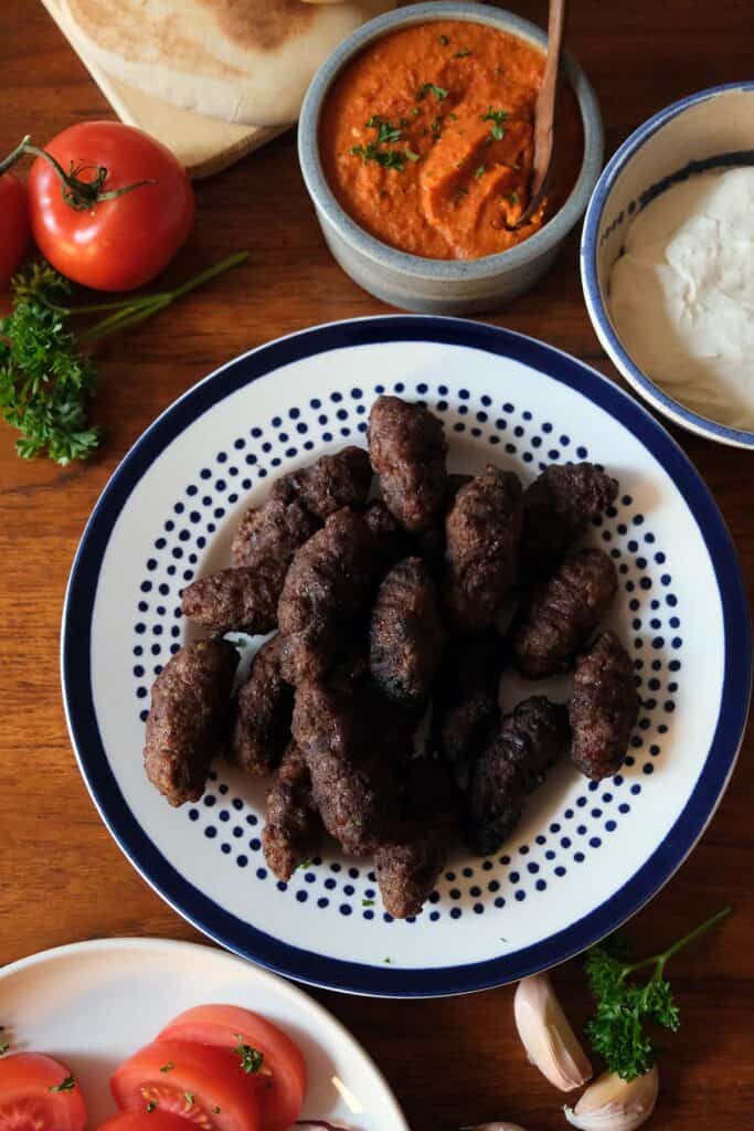 Traditional ćevapčići recipe platter with ajvar, kajmak, onions, and fresh bread
