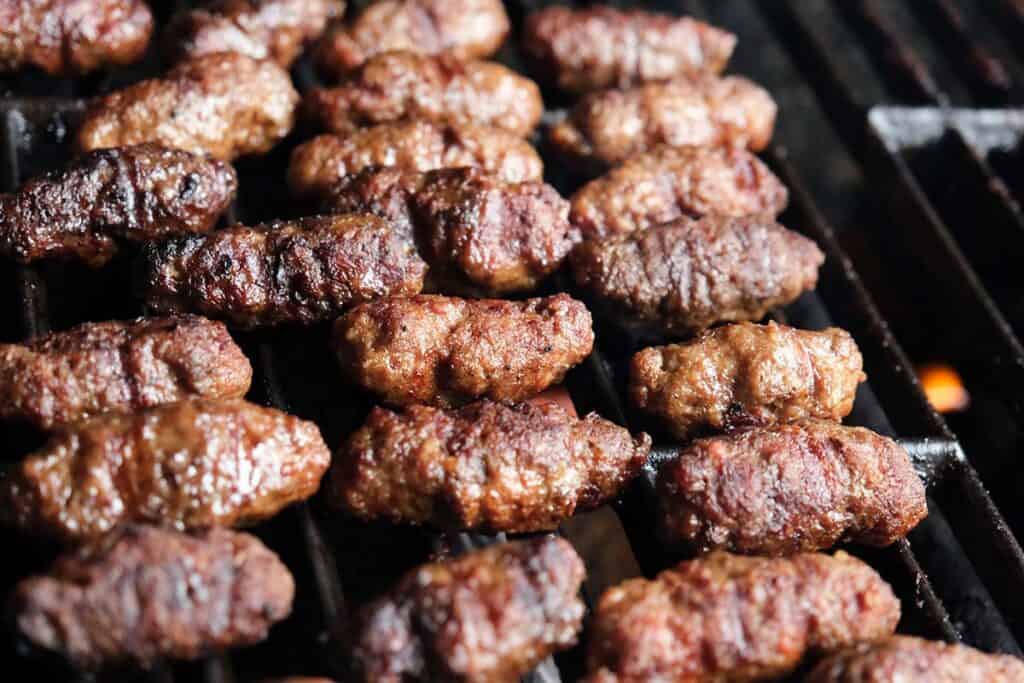 Close up of ćevapčići recipe cooking on grill with smoky char and juicy texture