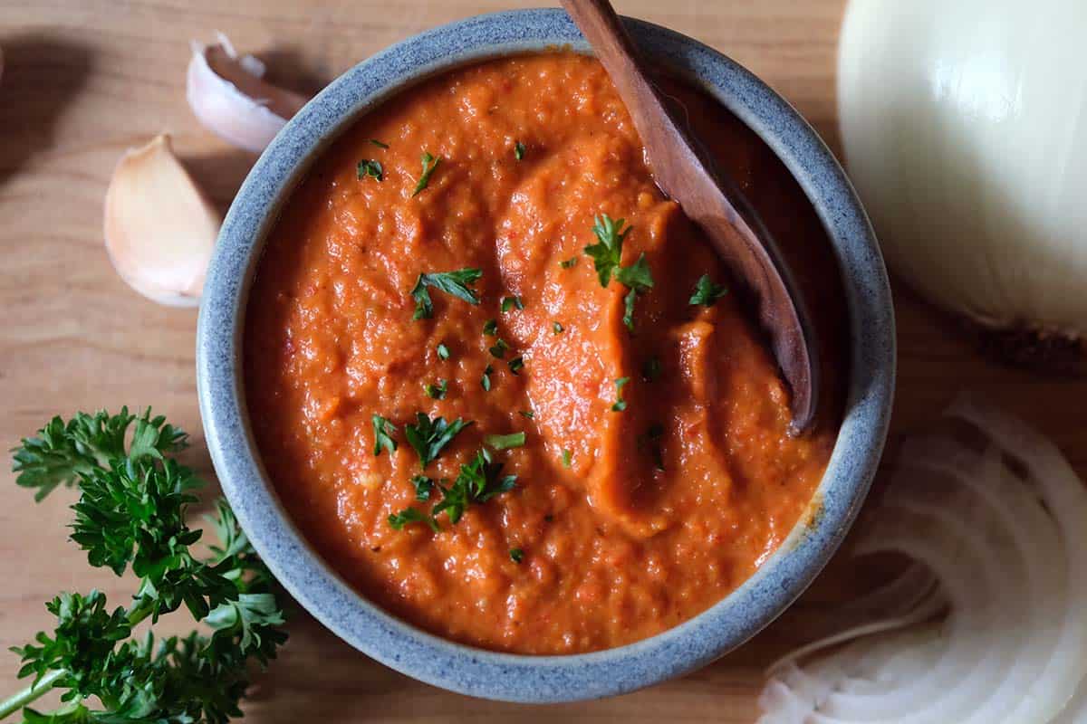 Top view of ajvar recipe Balkan red pepper sauce in a bowl with garlic and parsley garnish