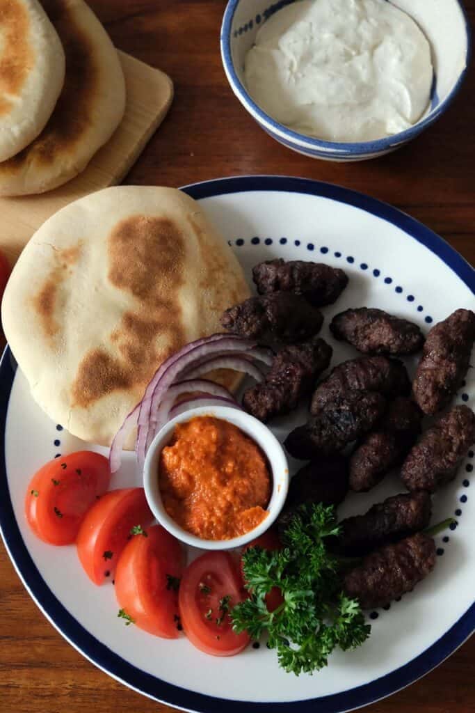Serbian ćevapčići recipe served with lepinja bread, ajvar, onions, and kajmak on a plate