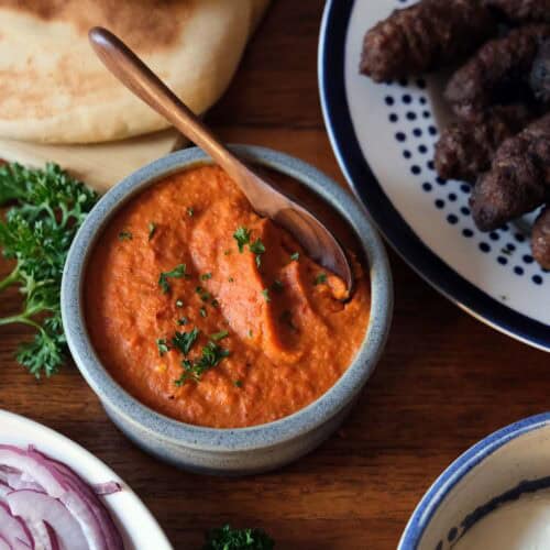 Ajvar recipe served with grilled cevapi, flatbread, sliced onions, and creamy sauce as a Balkan dish