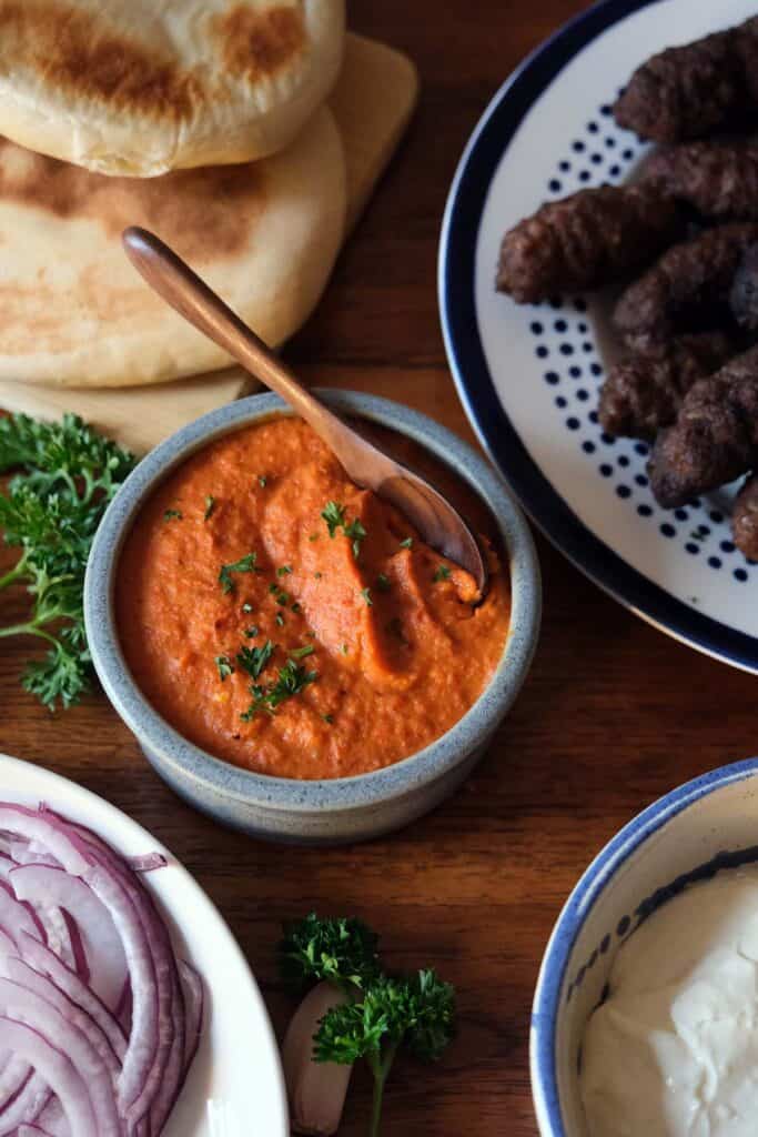 Ajvar recipe served with grilled cevapi, flatbread, sliced onions, and creamy sauce as a Balkan dish