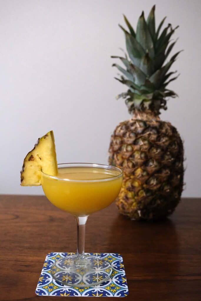 Easy pineapple coconut rum cocktail in elegant glasses with pineapple wedges, styled with whole pineapple behind