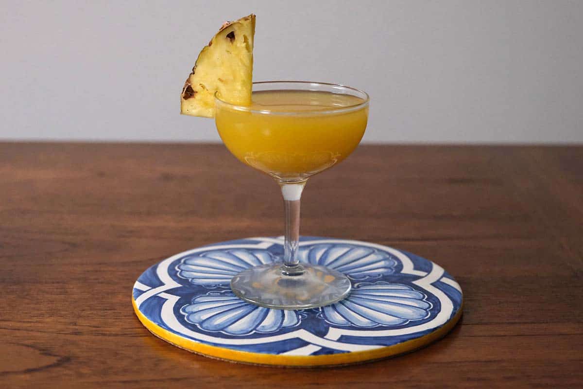 Tropical pineapple coconut rum cocktail with lime served in coupe glasses, bright golden color and fresh pineapple garnish